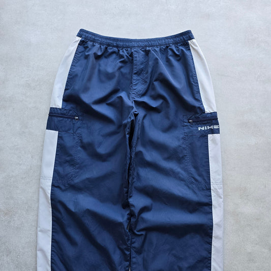 DEEP VINTAGE navy blue Nike track pants with white side panels, elastic drawstring waist, and zippered cargo pockets.