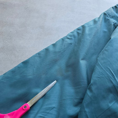 DEEP VINTAGE 90s Nike jacket sleeve showing a small mark on the teal fabric with scissors pointing to the spot